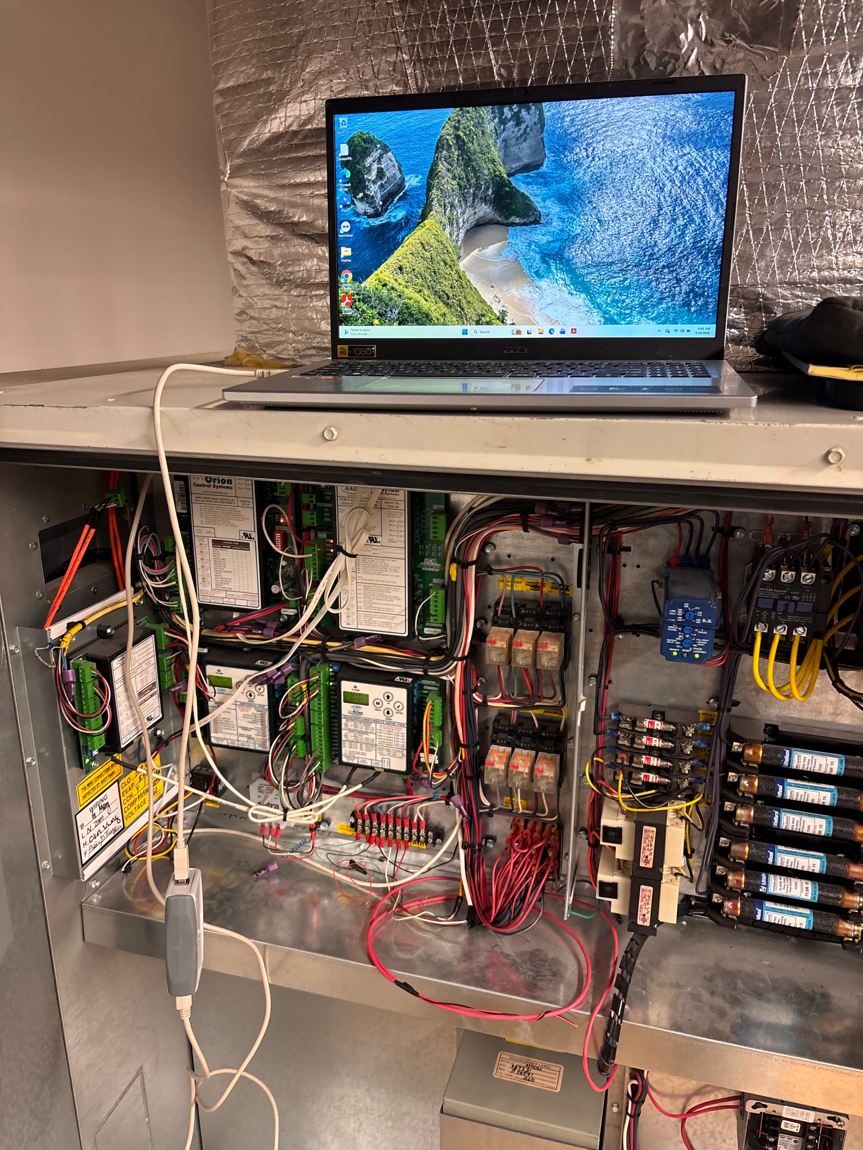Laptop connected to a complex industrial control panel with intricate wiring and electronic components.